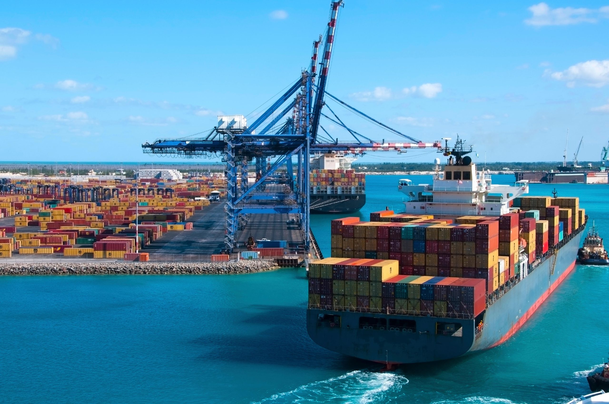 Port of Freeport Bahamas Container shipyard with heavy lifting Cranes and a ship coming in to dock assisted by tug boats